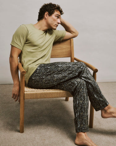 Man sitting on a chair wearing a cardamom shirt and patterned pants.